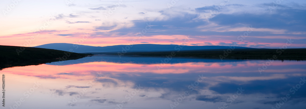 A beautiful sunset over a lake with a reflection of the sky in the water. The sky is a mix of pink and orange hues, creating a serene and peaceful atmosphere