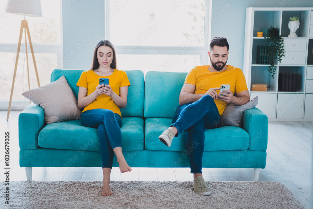 Full length portrait of two young people sit sofa use smart phone weekend pastime modern interior flat indoors Full length portrait of two young people sit sofa use smart phone weekend pastime modern interior flat indoors