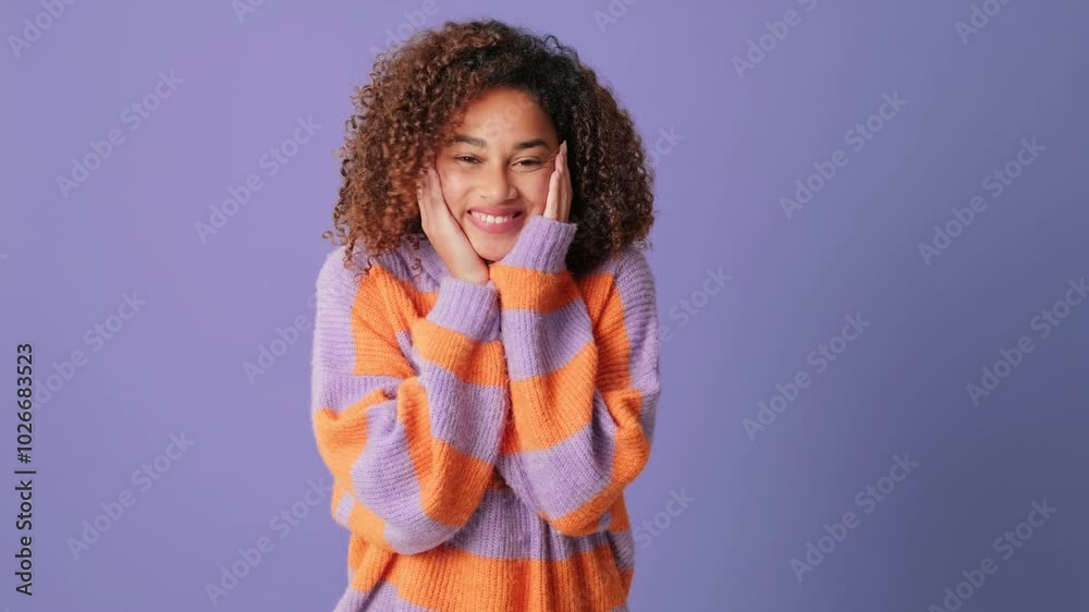 Happy young woman props up face with her hands looking at camera on lilac background in studio Happy young woman props up face with her hands looking at camera on lilac background in studio