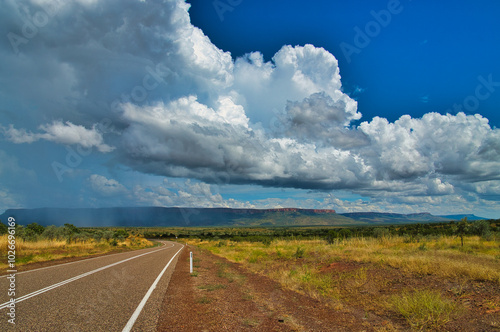 The road between El Questro and Kununurra in the remote north of Western Australia. Savanna landscape, table mountains, dramatic cloudscape and rain in the distance
 photo