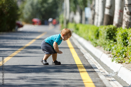 A young child crouching to explore the pavement in a sunny summer park