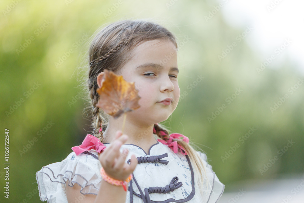 A girl enjoys a sunny summer day in the park, playfully holding a leaf while wearing a bright outfit and showing a cheeky expression A girl enjoys a sunny summer day in the park, playfully holding a leaf while wearing a bright outfit and showing a cheeky expression