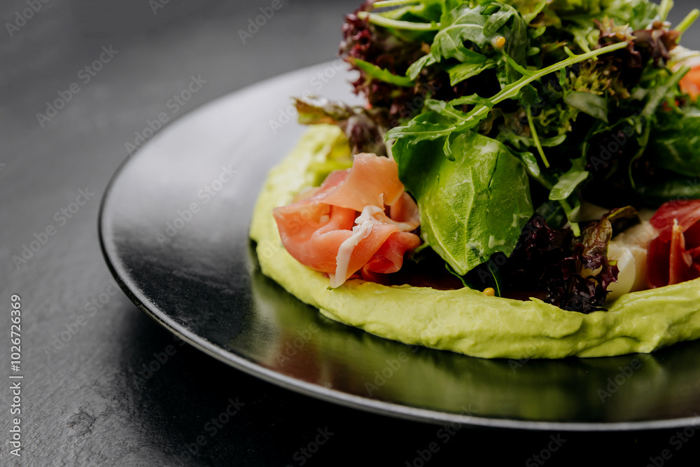 Fresh salad with avocado cream and prosciutto, served on a black plate, perfect for gourmet dining Fresh salad with avocado cream and prosciutto, served on a black plate, perfect for gourmet dining