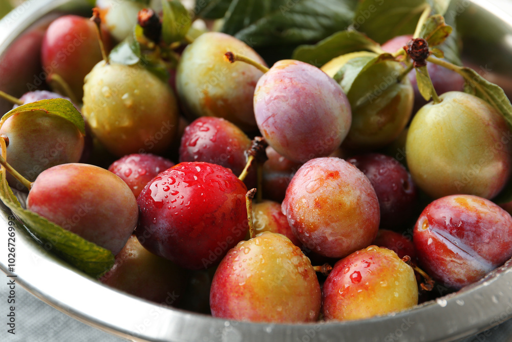 Ripe plums and leaves in colander on table, closeup Ripe plums and leaves in colander on table, closeup
