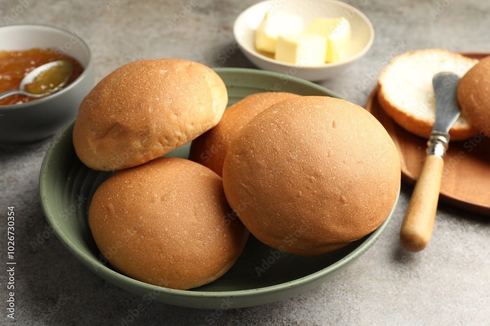 Fresh tasty buns, jam and butter on grey table, closeup Fresh tasty buns, jam and butter on grey table, closeup
