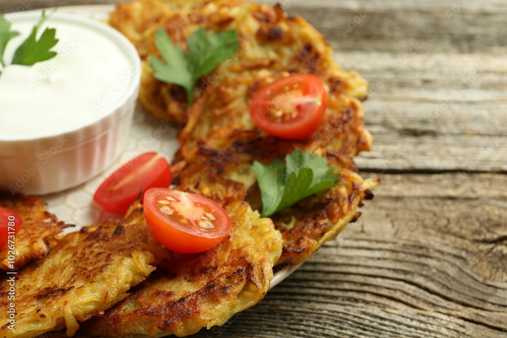 Delicious potato pancakes, sour cream, tomatoes and parsley on wooden table, closeup Delicious potato pancakes, sour cream, tomatoes and parsley on wooden table, closeup