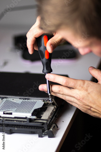 A man repairs a console, using a screwdriver to carefully open the device, focusing on its internal components and fan system.