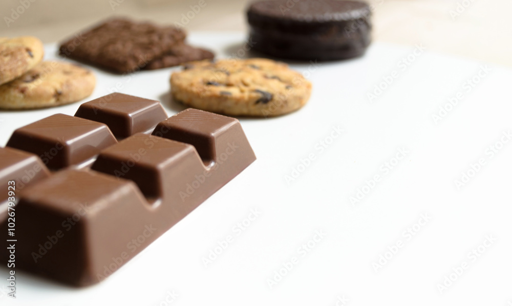 Barra de chocolate con galletas y alfajor argentino sobre mesa o superficie blanca. Barra de chocolate con galletas y alfajor argentino sobre mesa o superficie blanca.