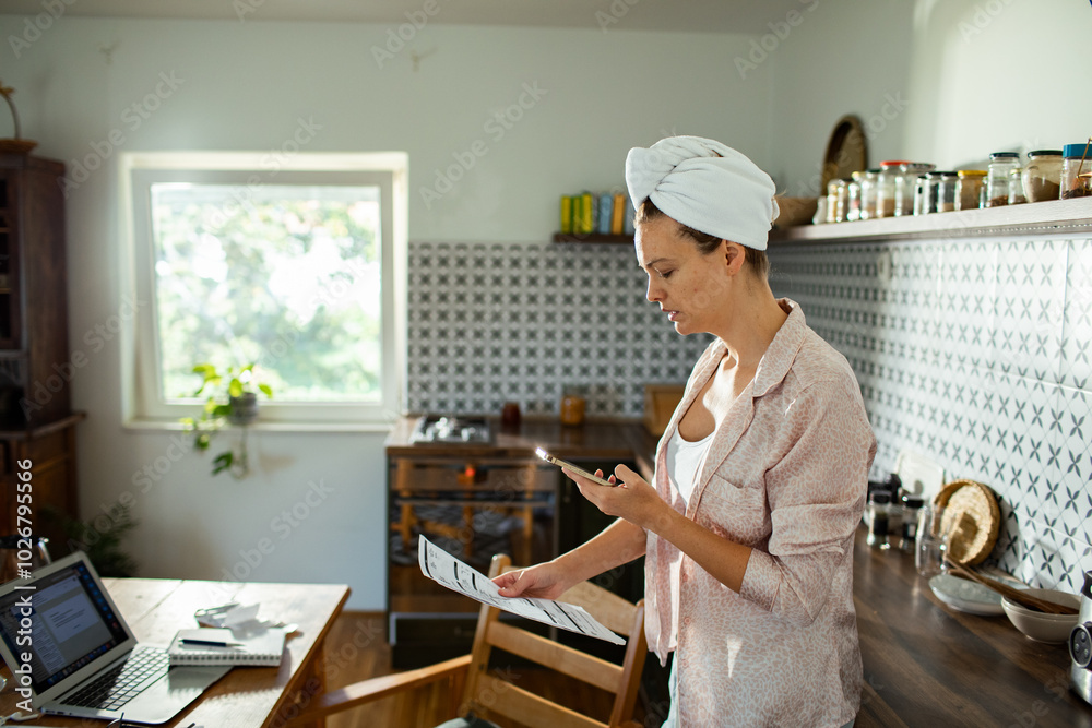 Serious woman working from home with laptop and bills in kitchen Serious woman working from home with laptop and bills in kitchen