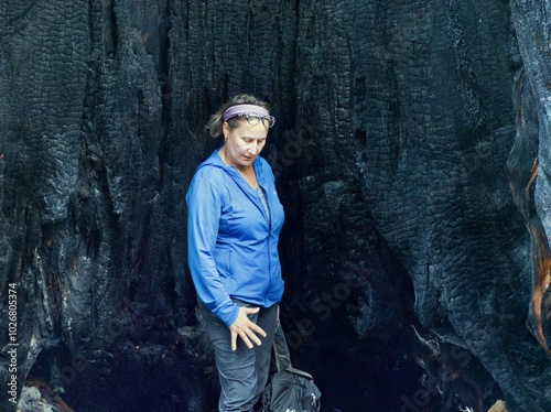 A woman in full body pose, looks down, while standing inside the burned and blackened hollow of a redwood tree. photo