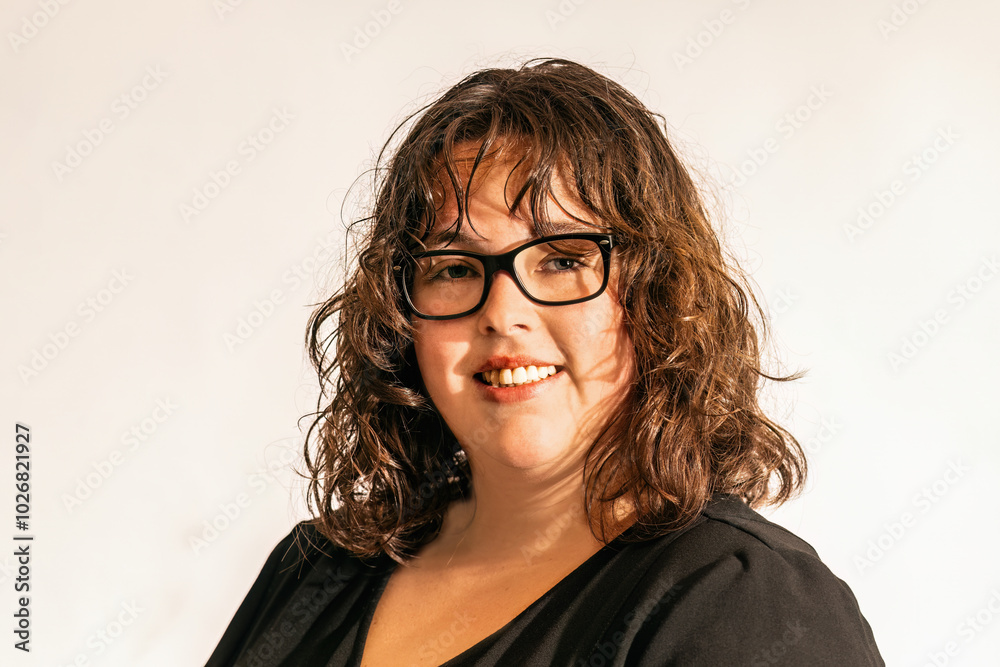 A young woman wearing glasses and a black dress in front of white studio background