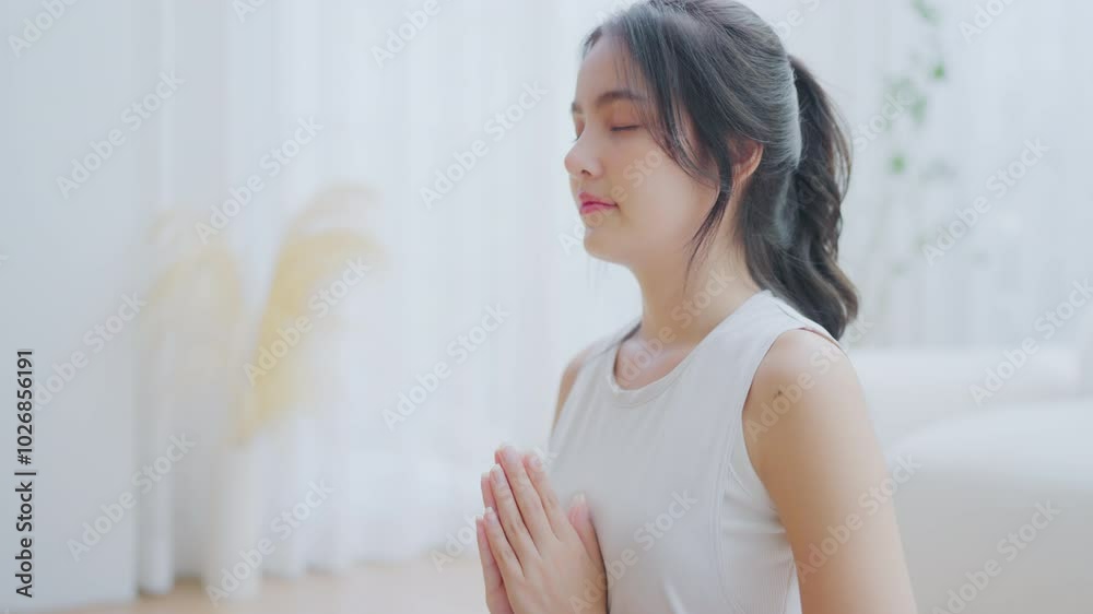 Happy young Asian woman practicing yoga and meditation at home sitting on floor in living room in lotus position and relaxing with closed eyes. Mindful meditation and wellbeing concept Happy young Asian woman practicing yoga and meditation at home sitting on floor in living room in lotus position and relaxing with closed eyes. Mindful meditation and wellbeing concept