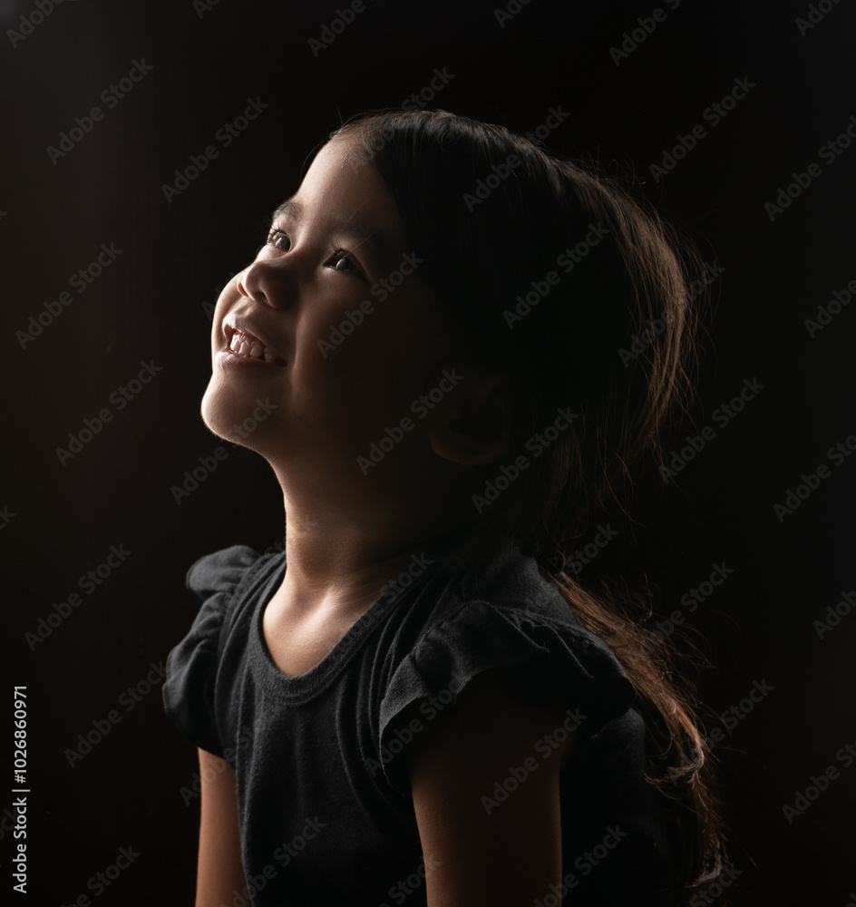 Obraz premium A delighted and joyful child gazes upwards, illuminated softly by gentle, warm lighting