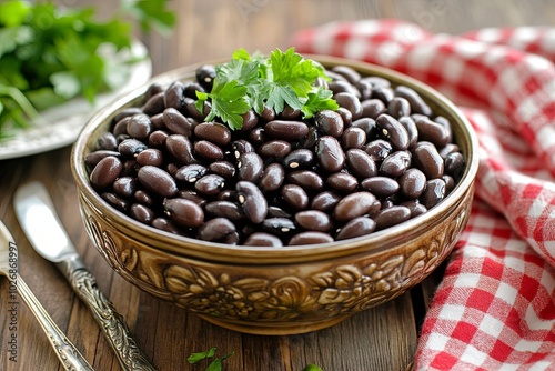 A bowl of cooked black beans with parsley garnish on a wooden table.