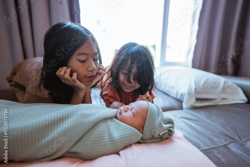 Two loving sisters gaze at their adorable newborn sibling wrapped in a soft blanket