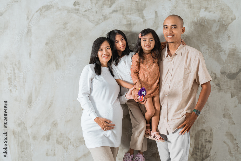 A cheerful family is happily posing together for a memorable picture in front of a colorful wall that adds charm to the image A cheerful family is happily posing together for a memorable picture in front of a colorful wall that adds charm to the image