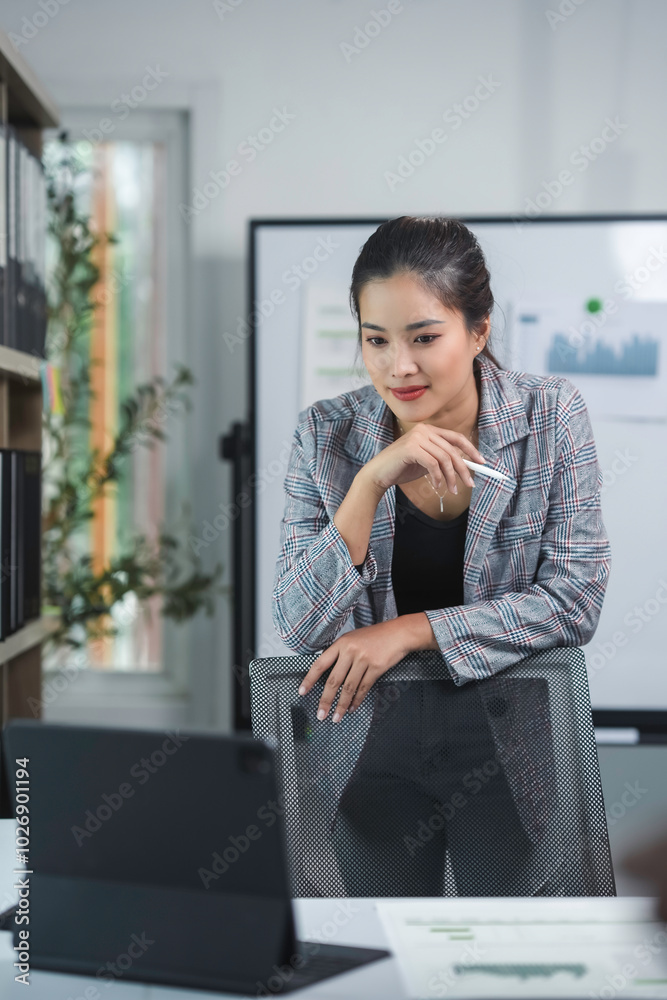 Young businesswoman is leaning on her chair in an office, holding a pen and looking at a tablet Young businesswoman is leaning on her chair in an office, holding a pen and looking at a tablet