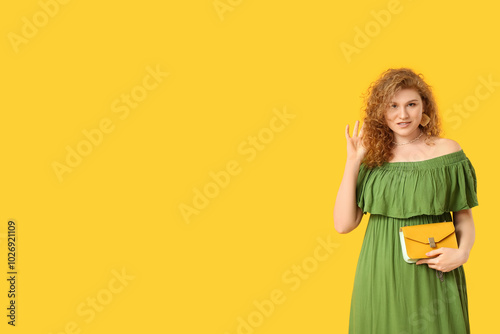 Beautiful young woman in stylish green dress with chain bag on yellow background