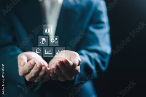 Control and business processes management concept. Businessman holding analytics icon on virtual screen for efficient operation and increased profits.