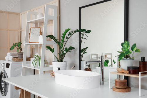 Modern sink, houseplants and cosmetic products on white table in bathroom