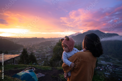 A woman is gently holding a small baby in her arms while gazing admiringly at the beautiful sunset in the distance on the horizon photo