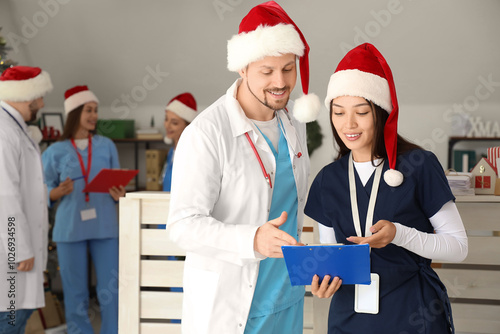 Young doctors in Santa hats with clipboard at hospital on Christmas eve