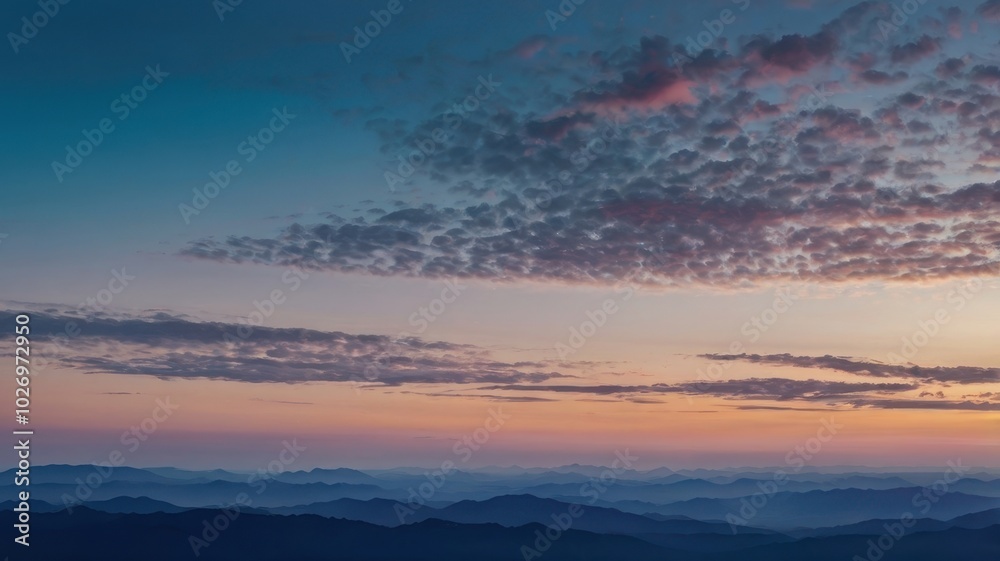 Fototapeta premium A breathtaking view of mountain ranges at sunset, with layers of blue hues and a warm orange sky. Silhouettes of mountains against a vibrant sunset sky