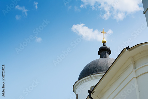 Black dome with a cross of an Orthodox church against a blue sky with white clouds