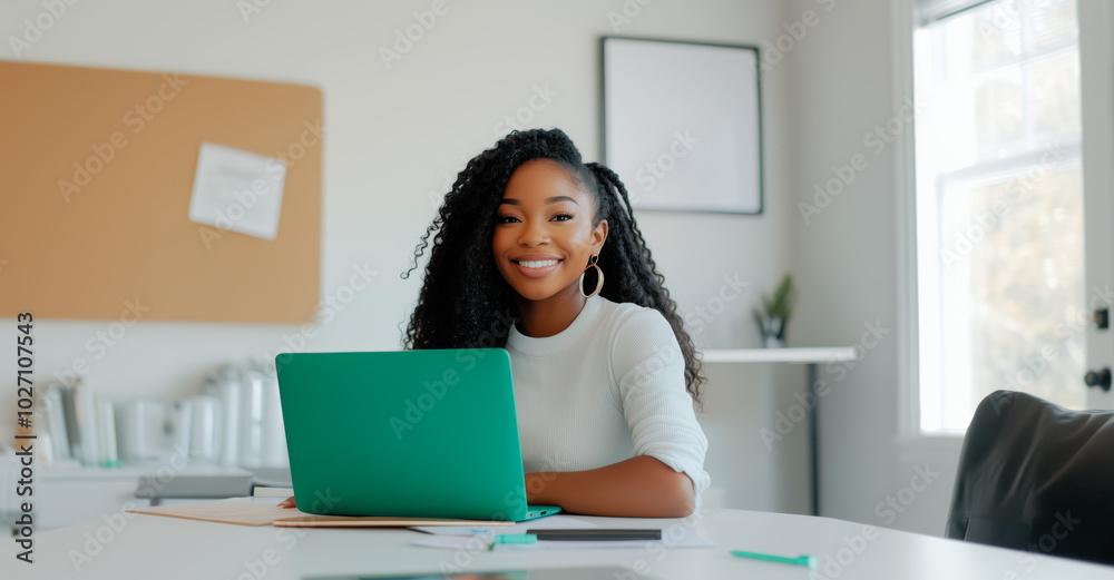 A cheerful woman sits at her desk with a laptop in a bright, modern office environment, looking focused and confident A cheerful woman sits at her desk with a laptop in a bright, modern office environment, looking focused and confident