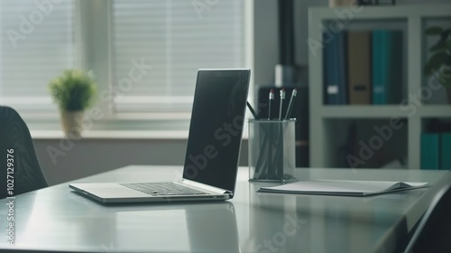 Front view laptop on white table. There is paper and a pen holder nearby. In modern office space