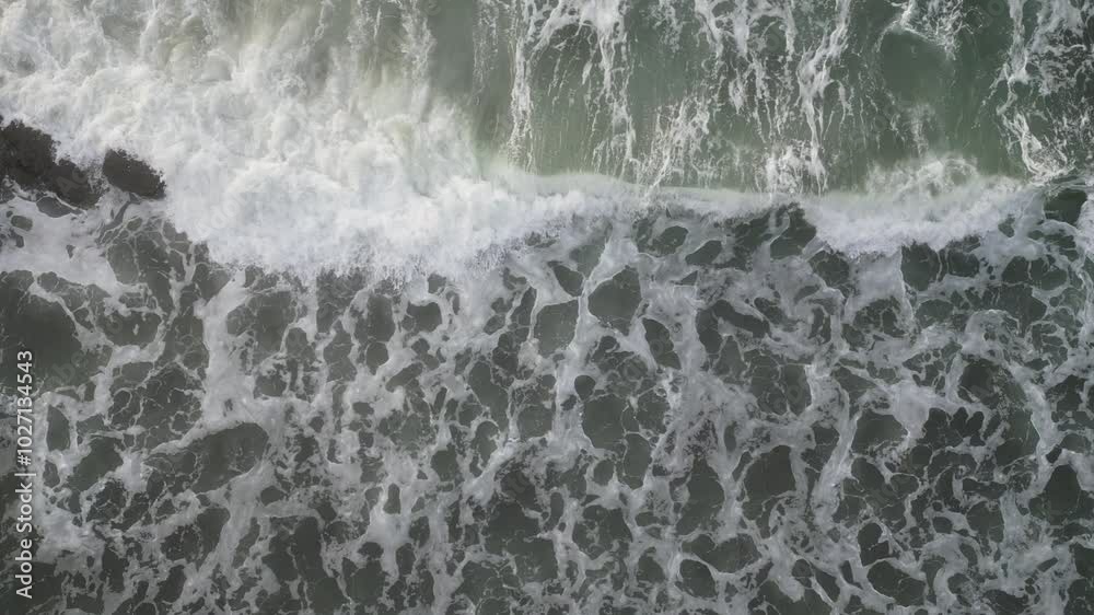 An Aerial view of White top waves crashing over rocks on the shoreline An Aerial view of White top waves crashing over rocks on the shoreline