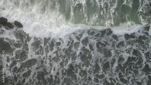 An Aerial view of White top waves crashing over rocks on the shoreline