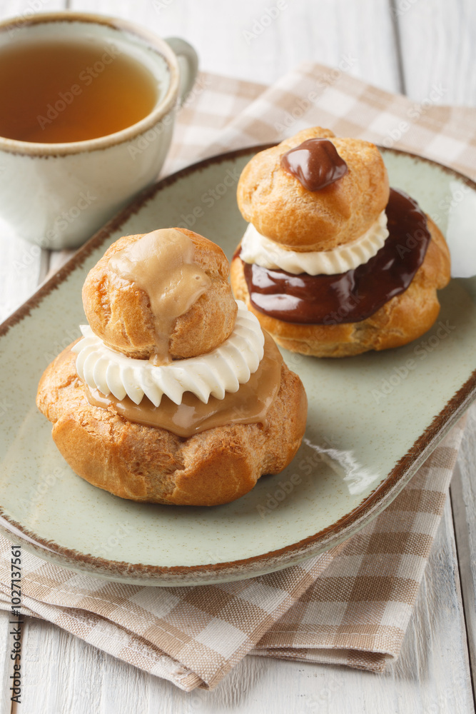 Religieuse pastry is composed of two choux buns filled with pastry cream, topped with chocolate ganache and decorated with cream closeup on the plate on the wooden table. Vertical
