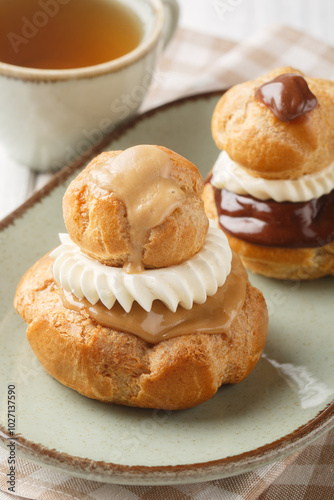 French Religieuse pastry profiteroles with custard cream and chocolate and coffee glaze close-up in a bowl on a wooden table. Vertical