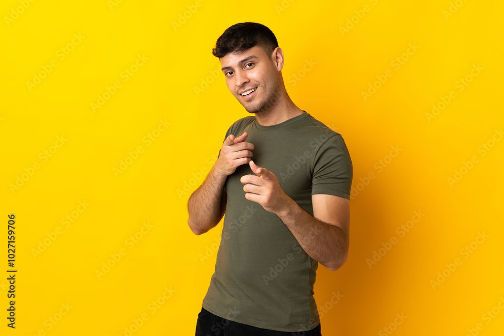 Young Colombian man isolated on yellow background surprised and pointing front Young Colombian man isolated on yellow background surprised and pointing front