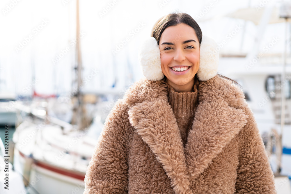 Young woman wearing winter muffs at outdoors keeping the arms crossed in frontal position Young woman wearing winter muffs at outdoors keeping the arms crossed in frontal position