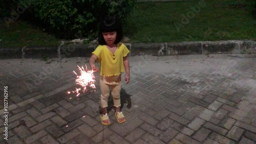 Little girl playing with fireworks sticks in the yard at night