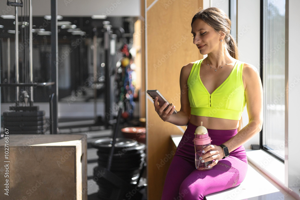 Fototapeta premium Fitness woman relaxing on mat use smartphone chatting at gym enjoy break