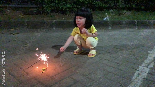 Little girl playing with fireworks sticks in the yard at night