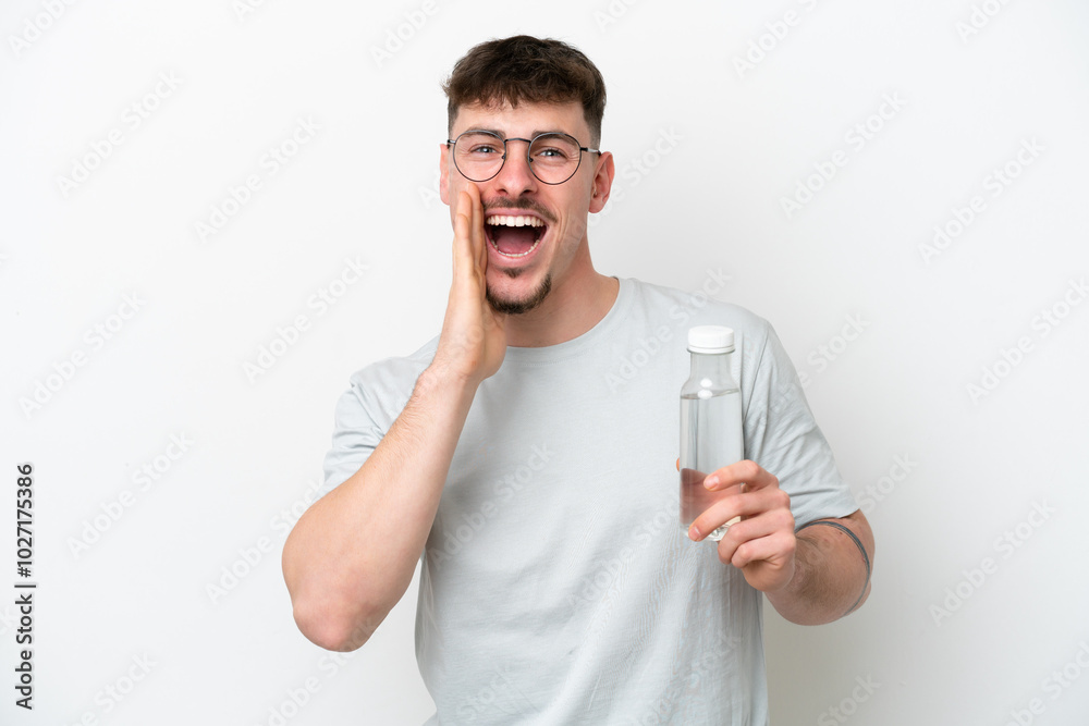 Young caucasian man holding a bottle of water isolated on white background shouting with mouth wide open Young caucasian man holding a bottle of water isolated on white background shouting with mouth wide open