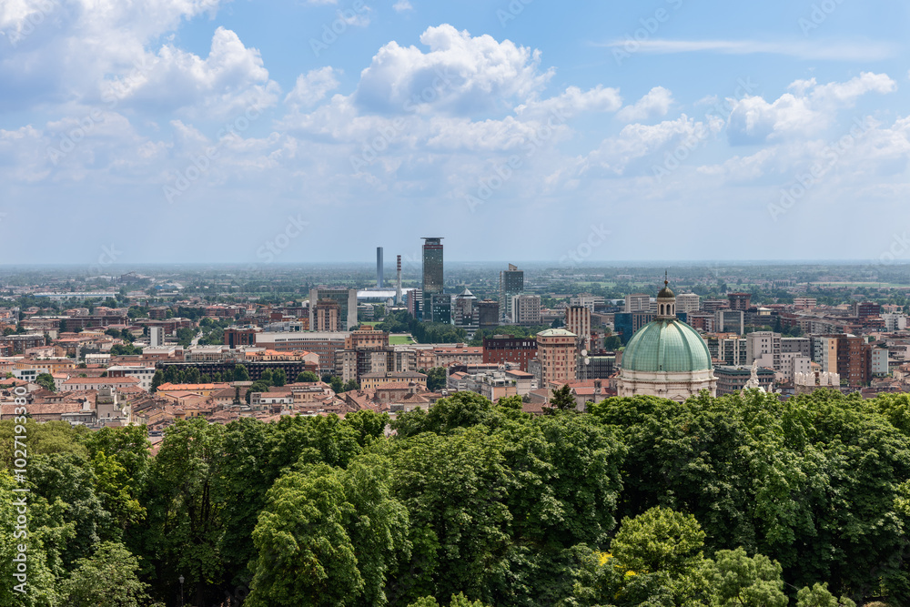 Fototapeta premium Brescia Duomo dome rises above the historic city center tiled rooftops with the business district visible in the distance. The scene highlights the city mix of ancient and contemporary structures