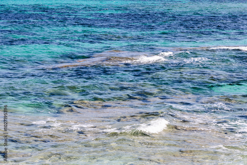 Fototapeta premium Texture of clear sea water with shades of turquoise and blue. The transparent water and gentle waves create a calming and visually appealing background, ideal for creative projects