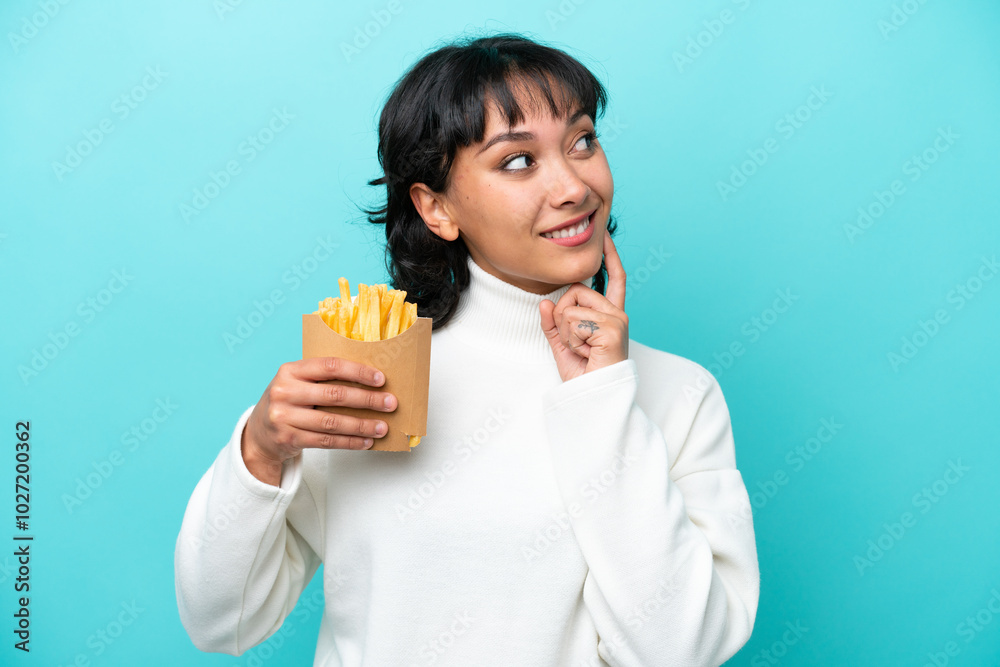 Young Argentinian woman holding fried chips isolated on blue background thinking an idea while looking up Young Argentinian woman holding fried chips isolated on blue background thinking an idea while looking up