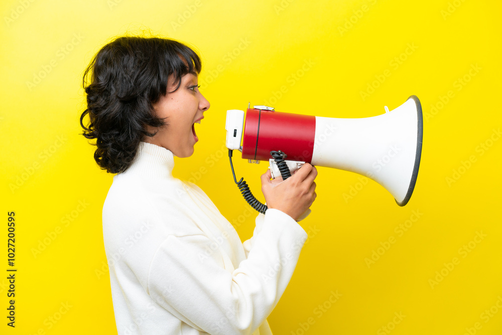 Young Argentinian woman isolated on yellow background shouting through a megaphone to announce something in lateral position Young Argentinian woman isolated on yellow background shouting through a megaphone to announce something in lateral position