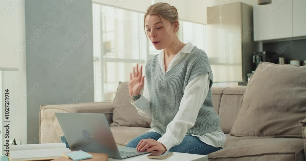 Smiling Woman Waving in a Virtual Meeting from Home, Engaging in a Friendly Online Conversation in a Bright, Modern Living Space