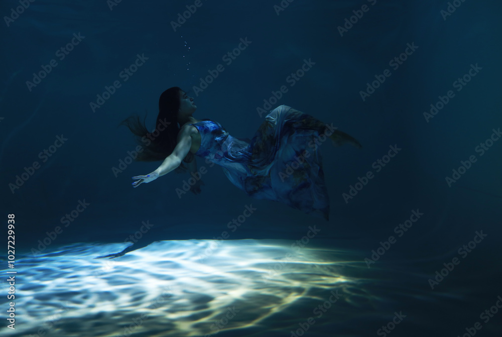 Fototapeta premium Beautiful woman in blue dress posing underwater as zero gravity in light beam