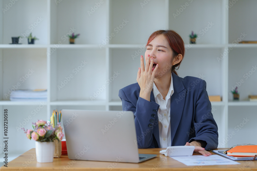 A young Asian businesswoman yawning while working with a laptop computer at the office is a woman in a casual office lifestyle concept. A young Asian businesswoman yawning while working with a laptop computer at the office is a woman in a casual office lifestyle concept.