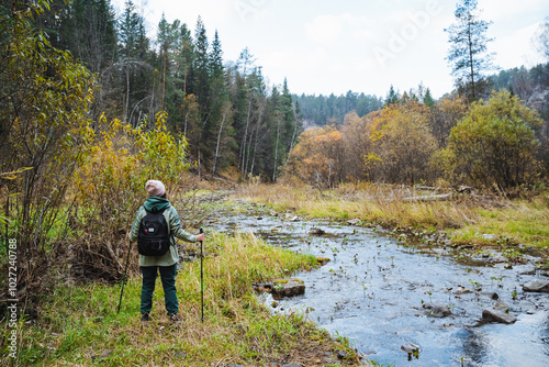 A Hiker is Enjoying Scenic Views Adjacent to a Tranquil Stream Surrounded by a Beautiful Autumn Forest Landscape, Filled with Colorful Leaves,