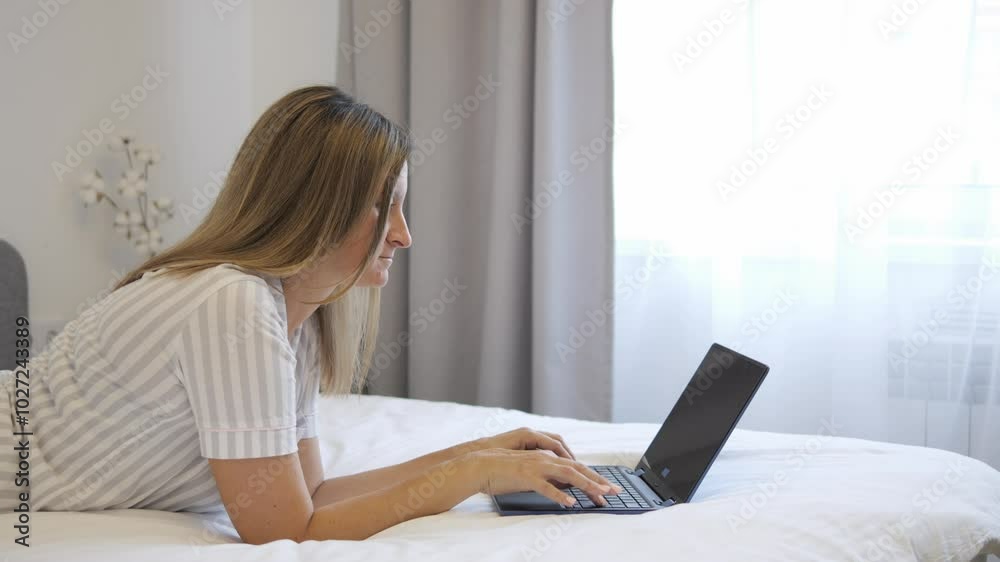 Woman comfortably works on laptop while lying on bed. She types and focuses on tasks, showing relaxed yet productive use of laptop. Video emphasizes remote work and laptop-based tasks in cozy setting. Woman comfortably works on laptop while lying on bed. She types and focuses on tasks, showing relaxed yet productive use of laptop. Video emphasizes remote work and laptop-based tasks in cozy setting.