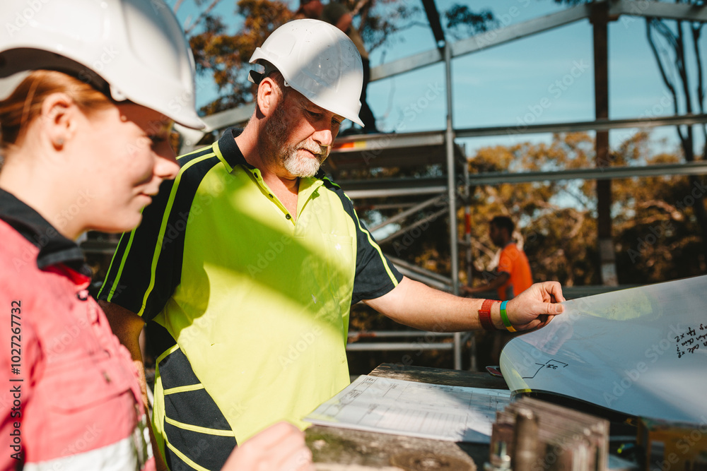© Austockphoto - Builders in hardhats looking at the blueprints on construction site